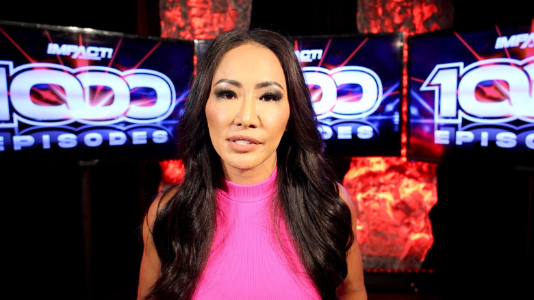 Gail Kim, standing in front of three large television screens