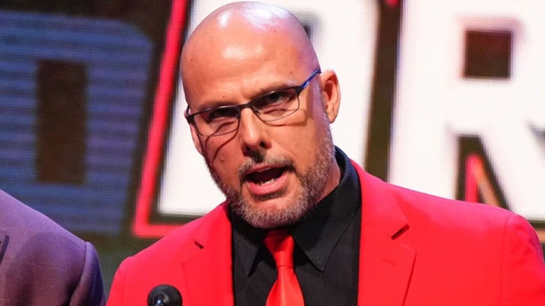 Adam Pearce delivers a message the audience on the stage during an episode of WWE programming.