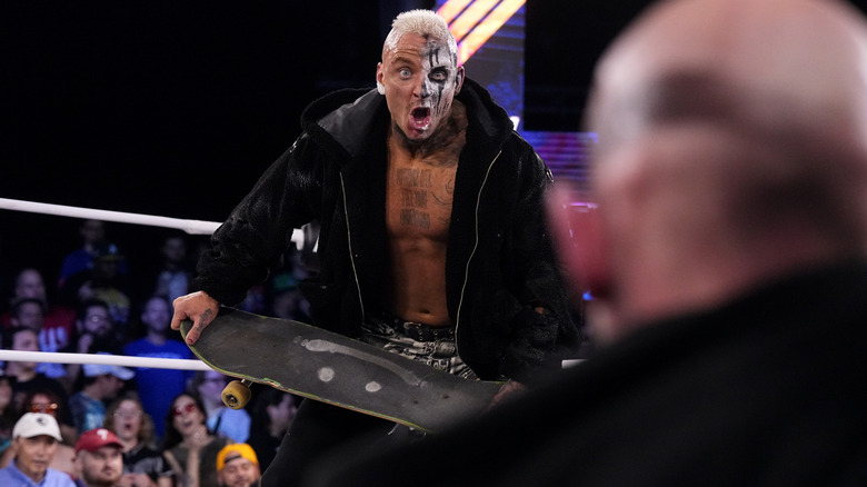 Darby Allin holding a skateboard with Jon Moxley in the foreground