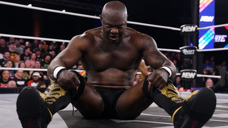 Shelton Benjamin sits open-legged towards the camera, and glares at the lens through his forehead.