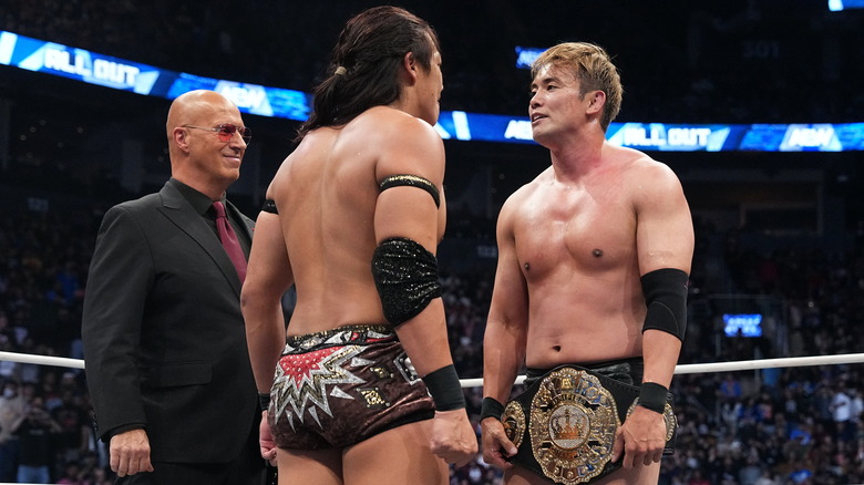 Don Callis stands behind Konosuke Takeshita and Kazuchika Okada after Okada's successful Unified Championship at AEW All Out.