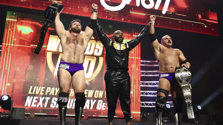 Stokely Hathaway raises the hands of AEW World Tag Team Champions FTR on the stage following their victory at 
