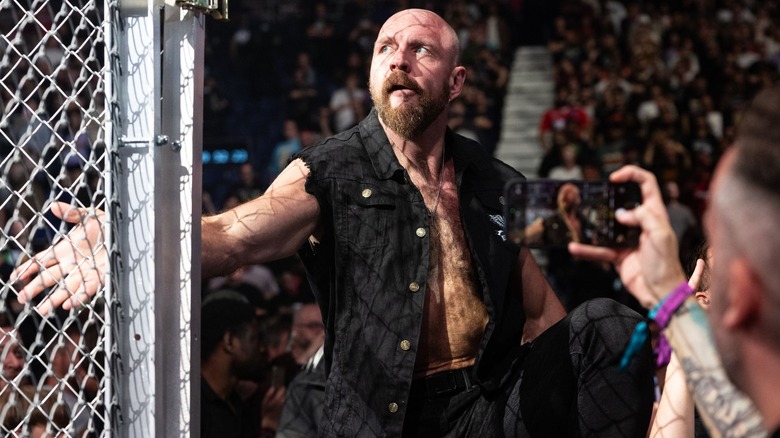 Jon Moxley scoffs as he runs his hand over the chain-link wall of a steel cage.