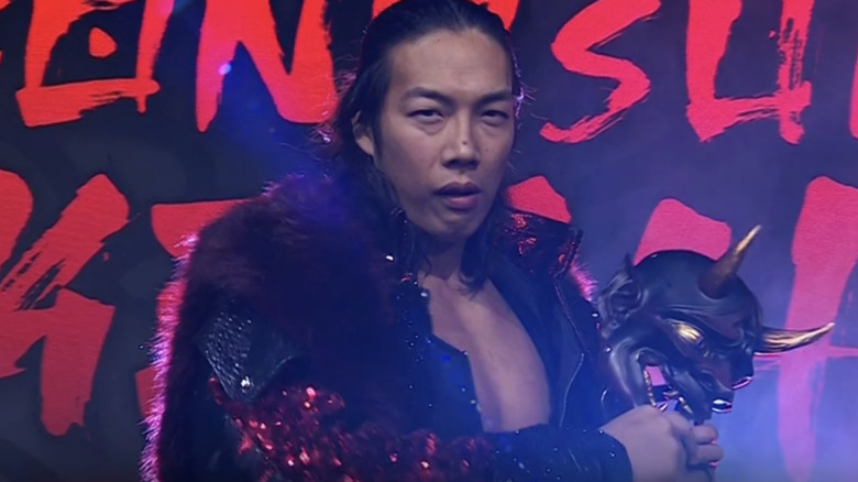 Konosuke Takeshita stares into the camera, mask in hand, during his entrance