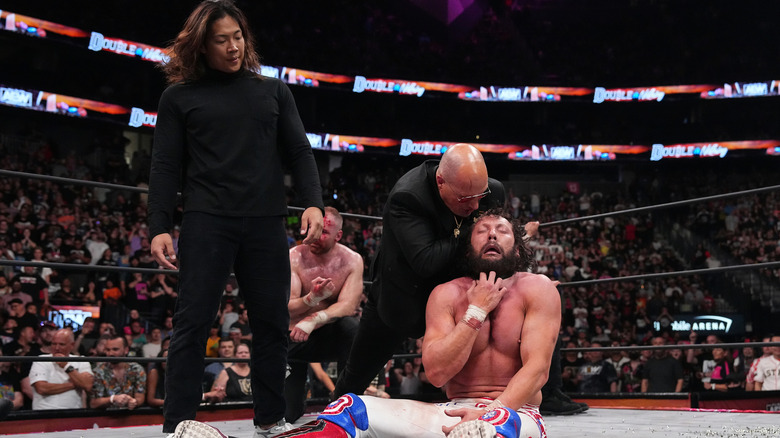 Don Callis chokes Kenny Omega while Konosuke Takeshita and Jon Moxley watch