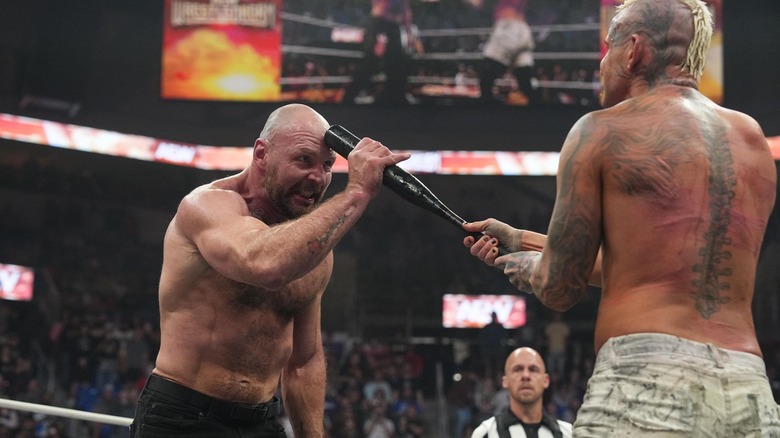 Jon Moxley stares down Darby Allin, pushing Darby's baseball bat into his forehead.
