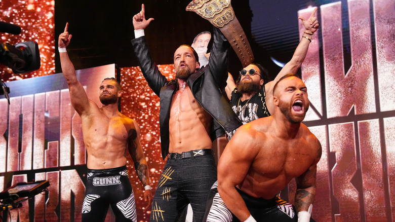 Bullet Club Gold with finger guns and belts in the air