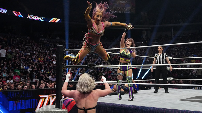 Mina Shirakawa jumps from the top rope to take out Toni Storm below, as AZM looks on from inside the ring.
