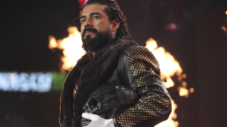 Andrade El Idolo heads down to the ring, mask under his arm, pyro going off behind him, at AEW Dynasty 2026.