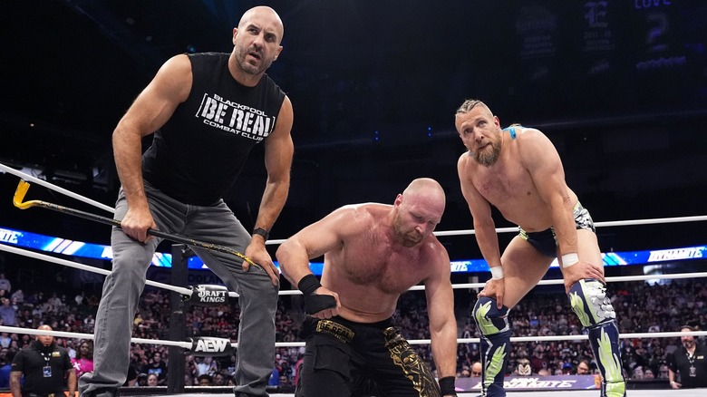 Claudio Castagnoli and Bryan Danielson flank a downed Jon Moxley.