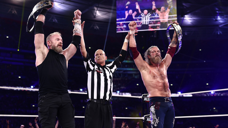 A referee holds up the arms of Christian Cage and Adam Copeland after their victory at AEW All In London 2026.