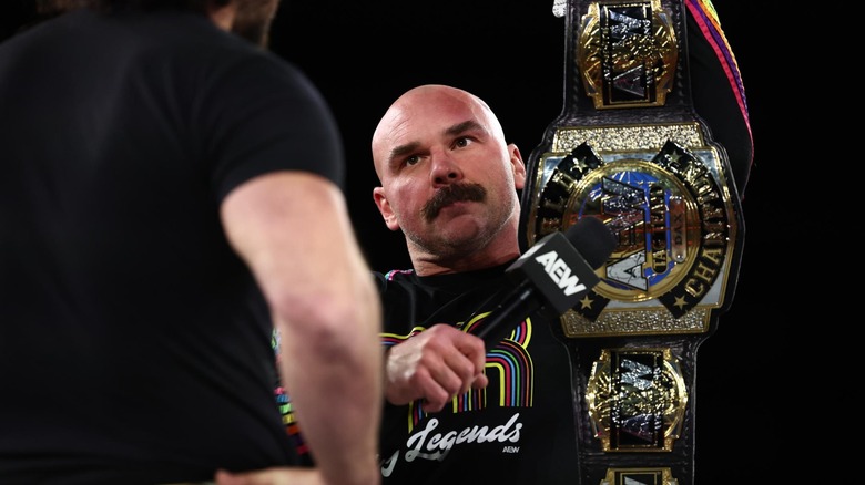 Dax Harwood holds a microphone up to his title belt