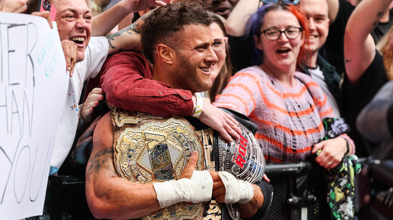 MJF celebrates with his two title belts, surrounded by fans.