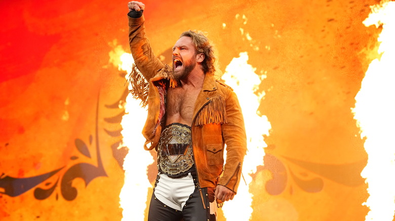 AEW World Champion "Hangman" Adam Page poses on the stage, fire blasting behind him, ahead of a match on "AEW Dynamite."