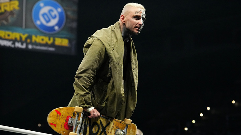Darby Allin holding a skateboard near the ring ropes