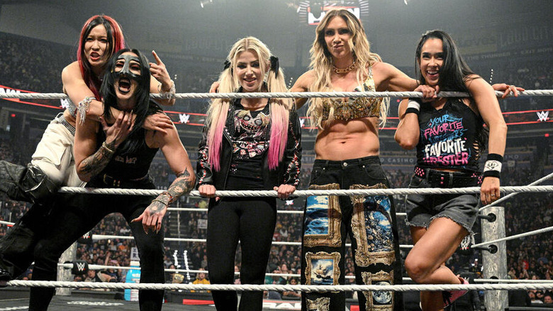 IYO SKY, Rhea Ripley, Alexa Bliss, Charlotte FLair, and AJ Lee stand alongside each other in the ring.