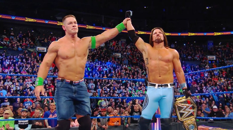 John Cena levanta la mano de AJ Styles en señal de victoria.