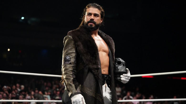 Andrade looks to the crowd from the ring, his mask in hand, ahead of a match on 