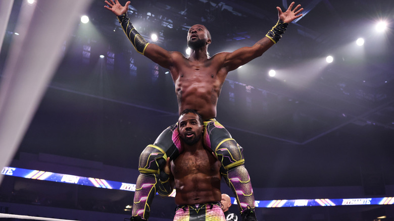 Kofi poses on Austin Creed's shoulders during their debut match on 