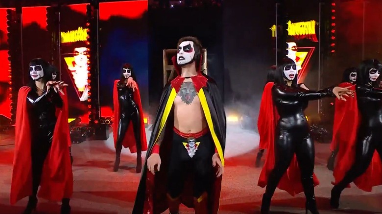 Danhausen emerges from the crate on the stage at WWE Elimination Chamber, accompanied by backstage dancers dressed in bodysuits and matching face paint.