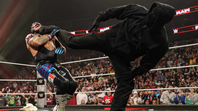 A masked figure superkicking Rey Mysterio
