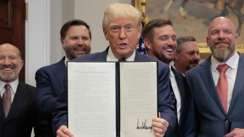 Donald Trump holding up a bill while men behind him laugh