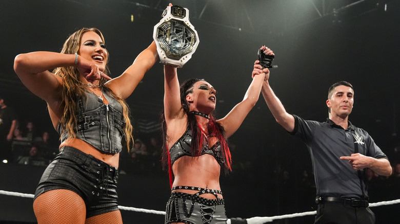 Jacy Jayne having her arms raised by Fallon Henley and a referee