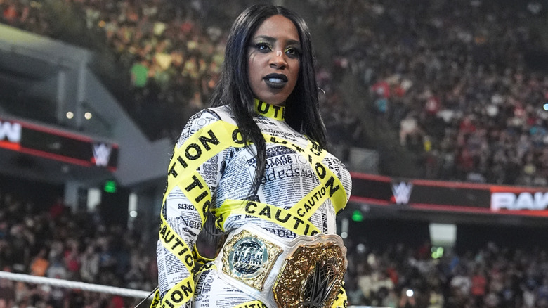 Naomi wearing the Women's World Championship, caution tape, and newspaper