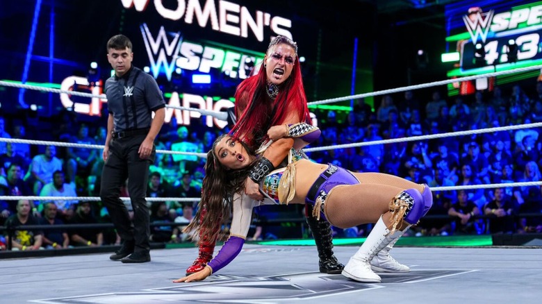WWE Women's Speed Champion Wren Sinclair looks toward the camera, shocked expression on her face, as Zaria puts her in a submission hold during a match for the Speed title on "WWE NXT."