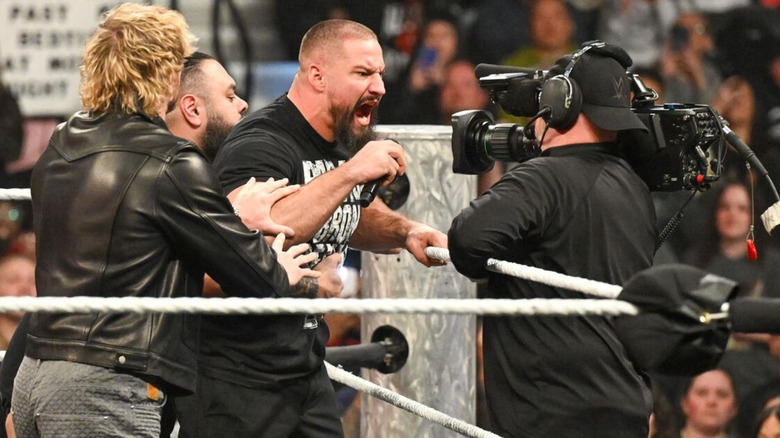 Bron Breakker cuts a promo into a camera, as Logan Paul and Bronson Reed attempt to hold him back, during an episode of 