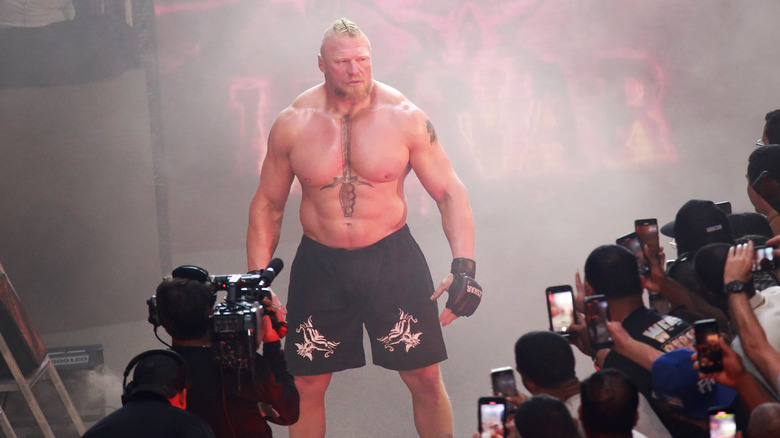 Brock Lesnar looks on in a black blazer, blue and white button-up shirt, and white undershirt.