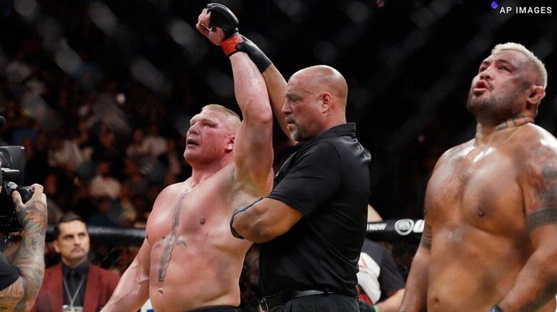 A referee raises Brock Lesnar's hand in the cage, as they stand alongside Mark Hunt, at UFC 200.