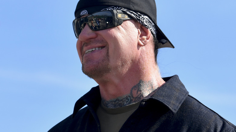 The Undertaker wearing a hat and sunglasses smiling