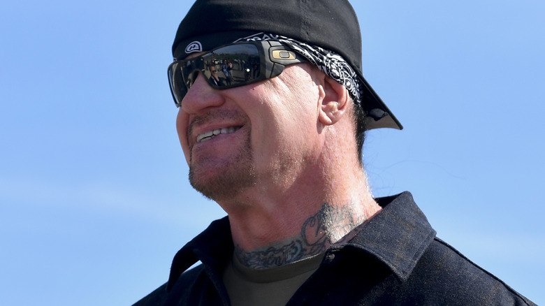 The Undertaker wearing a hat and sunglasses smiling