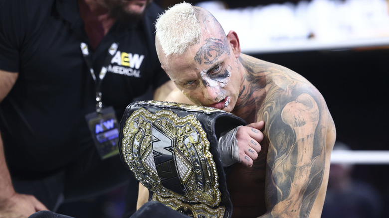 Darby Allin clutches the AEW World Championship to his chest while sitting in the ring following a victory on 