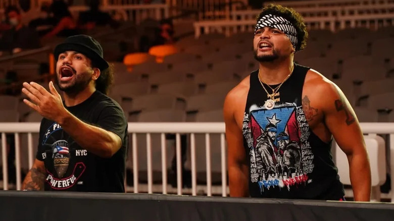 Ortiz and Mike Santana yell to the ring from the empty crowd in an area during an AEW show.