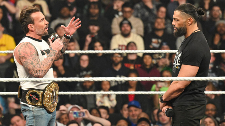 CM Punk is holding a microphone and talking to Roman Reigns
