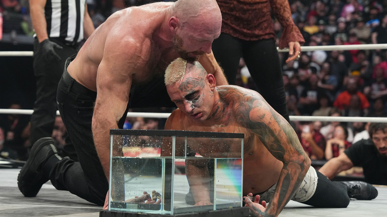 Jon Moxley holds Darby Allin up above a fish tank filled with water in the middle of the ring during their 