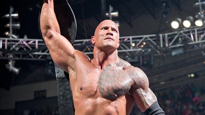 The Rock holding the WWE Championship above his head at the top of the turnbuckle as he looks out toward the audience.