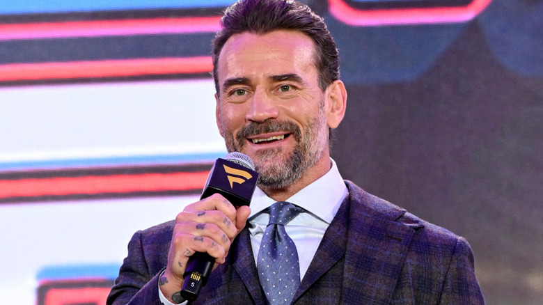 CM Punk is holding a microphone and talking to Roman Reigns