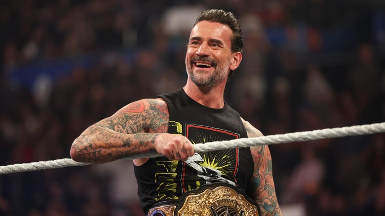 The WWE World Heavyweight Champion CM Punk smiles on the apron of the ring as he heads in to speak with Cody Rhodes and Roman Reigns