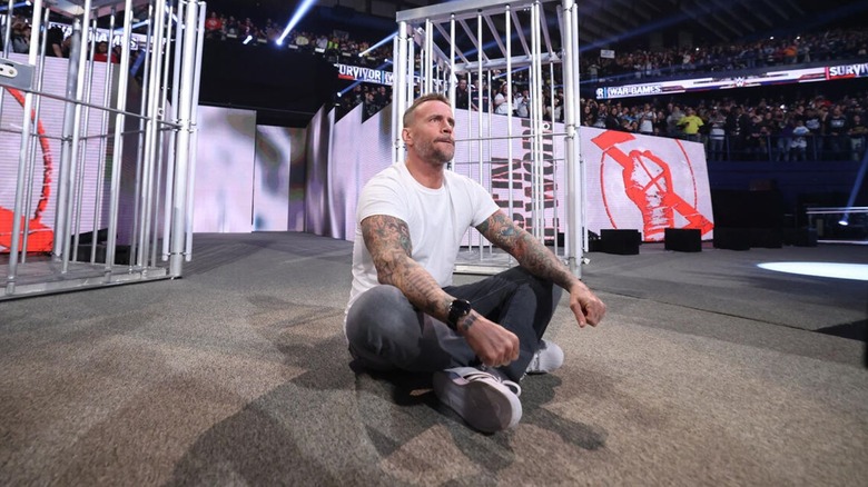 CM Punk sits cross-legged on the stage as the crowd explodes during his return to WWE at Survivor Series in 2023.