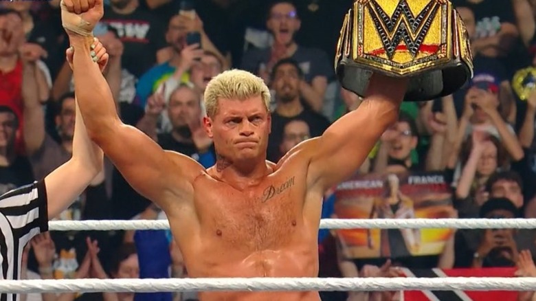 Cody Rhodeshas his hand raised in the ring, holding WWE title in his other hand
