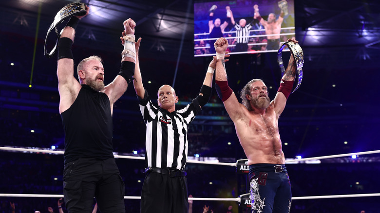 A referee raises the hands of Adam Copeland and Christian Cage as they hold the AEW World Tag Team Championships high after their victory at AEW All In: London 2026.