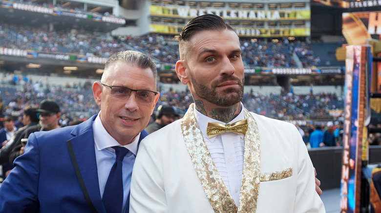 Corey Graves, in white, poses next to Michael Cole, in blue