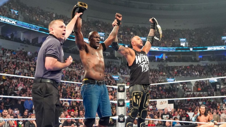 A referee holds up the arm of R-Truth as he grasps Damian Priest after a successful retention of the WWE Tag Team Championships.
