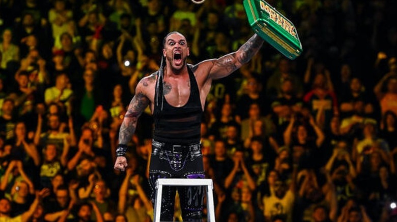 Damian Priest holds up the Money in the Bank briefcase atop a ladder after winning the contract at the premium live event.