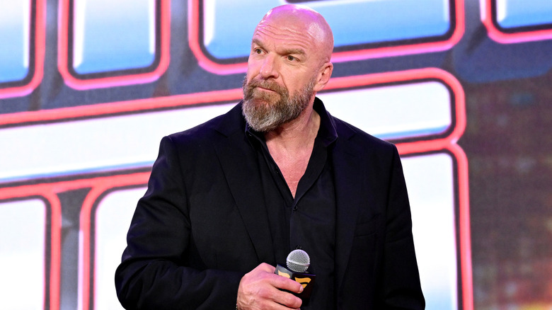 Paul Levesque carrying a microphone in a black suit