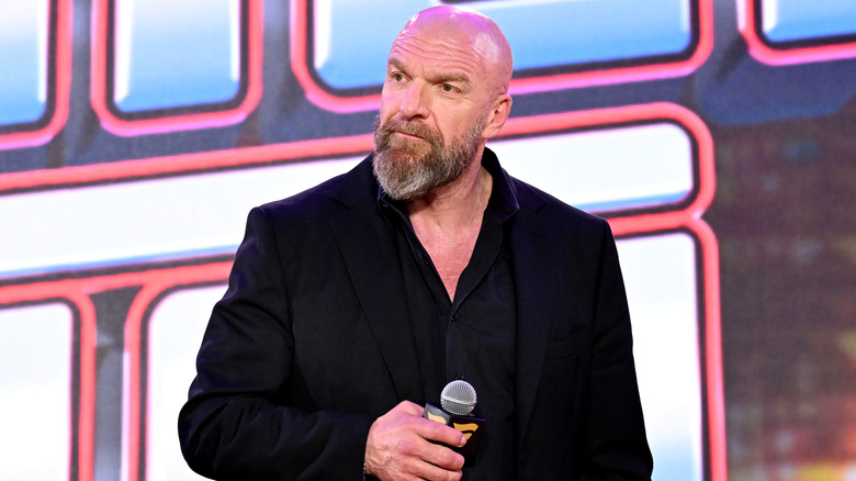 Paul Levesque wearing a black shirt and holding a mic