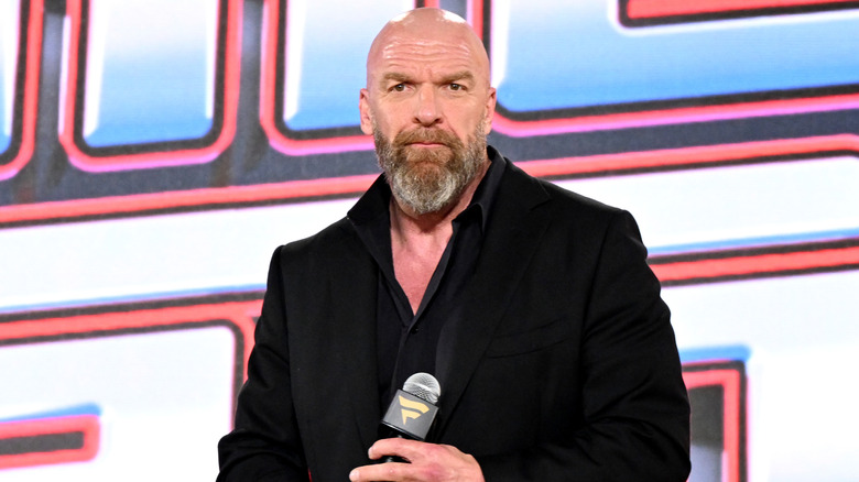 Paul Levesque in a black suit holding a Fanatics mic